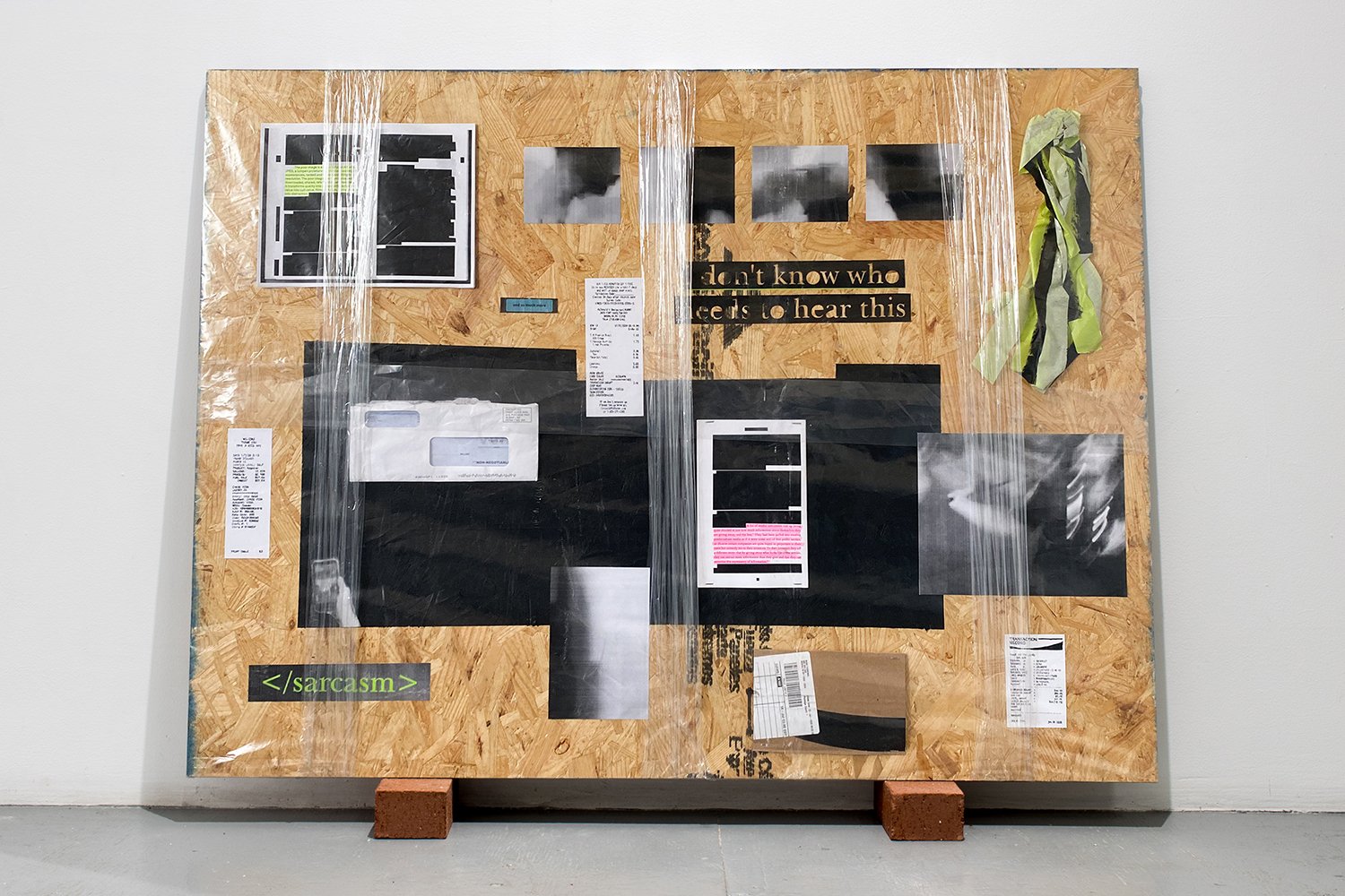 Mixed-media assemblage on an OSB panel combining receipts, envelopes, photographs, printed text, black painted areas, plastic wrap, and a fluorescent safety garment.