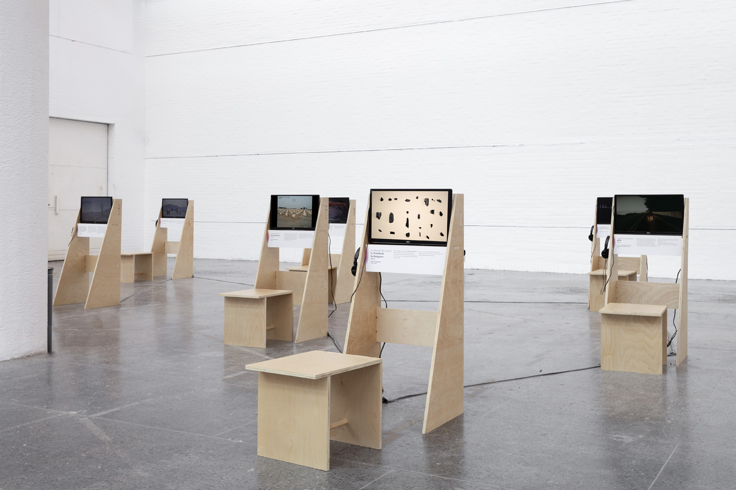 Installation view of Projected Ecologies with several plywood video stations and stools arranged across the gallery.